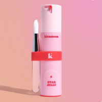 Pink cosmetic dispenser with a brush bundled to the side by a red silicone band. The silicone band has the product logo in pink print to match the bottle.