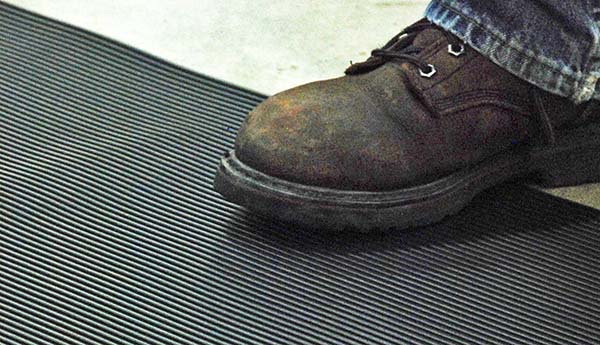 Worker's boot stepping on black ribbed matting